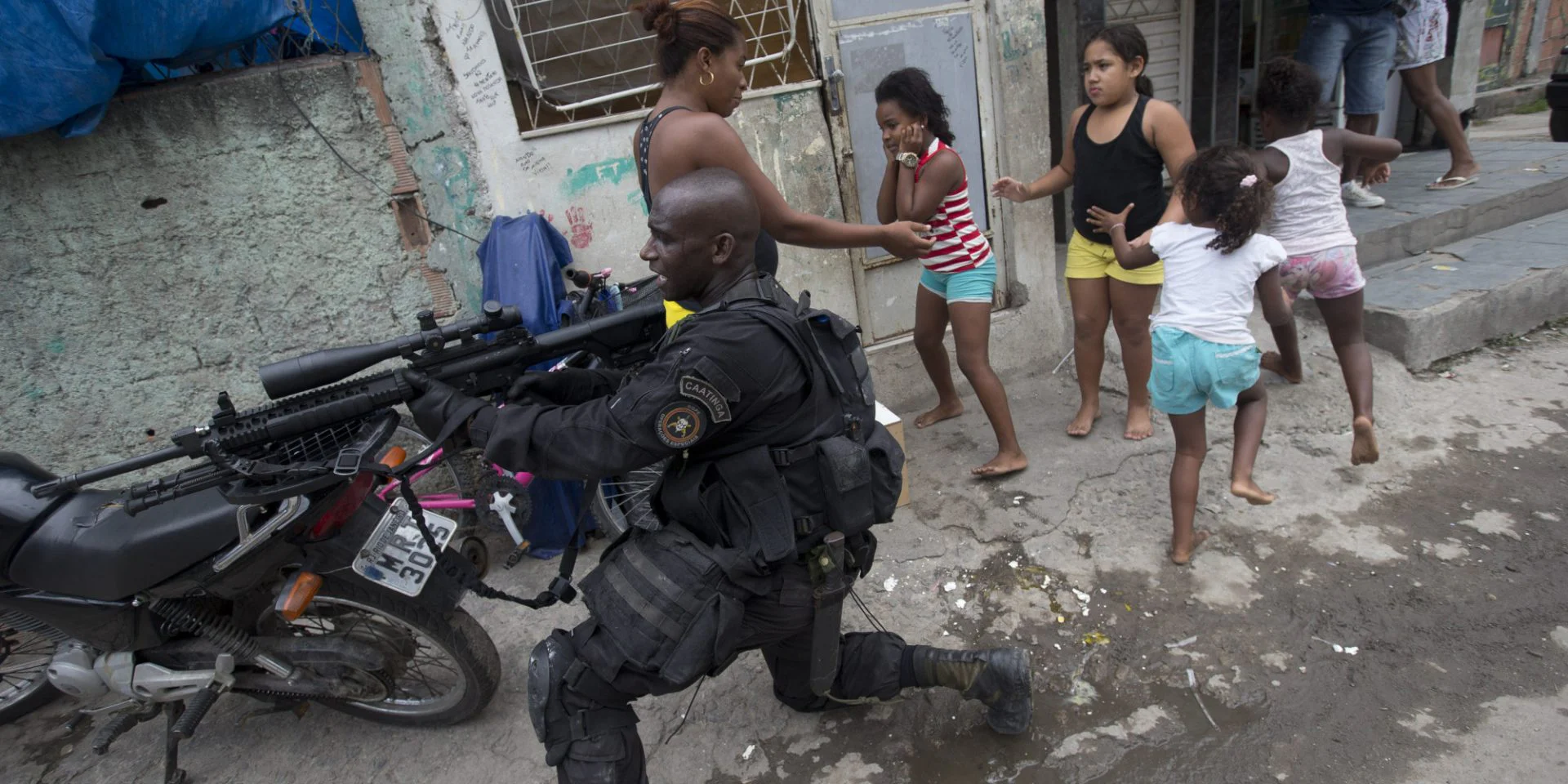 IGOR VIDOR 4 Special Police Operations Battalion (BOPE) officer takes position while residents run for cover during an operation in the Mare slum complex, ahead of its "pacification," in Rio de Janeiro, Brazil, Wednesday, March 26, 2014.